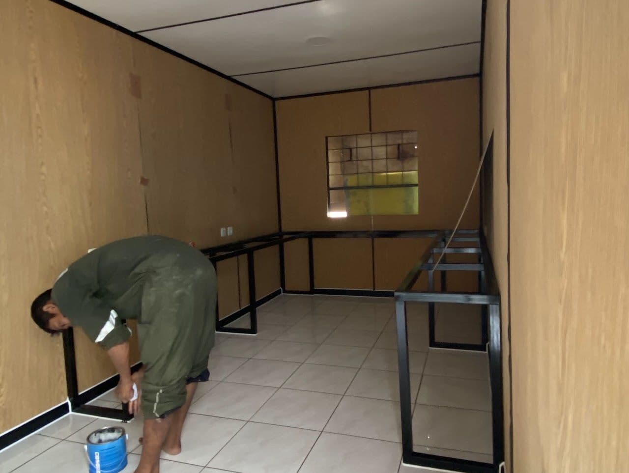 Pekerja mengecat rangka meja di dalam container berdinding kayu
